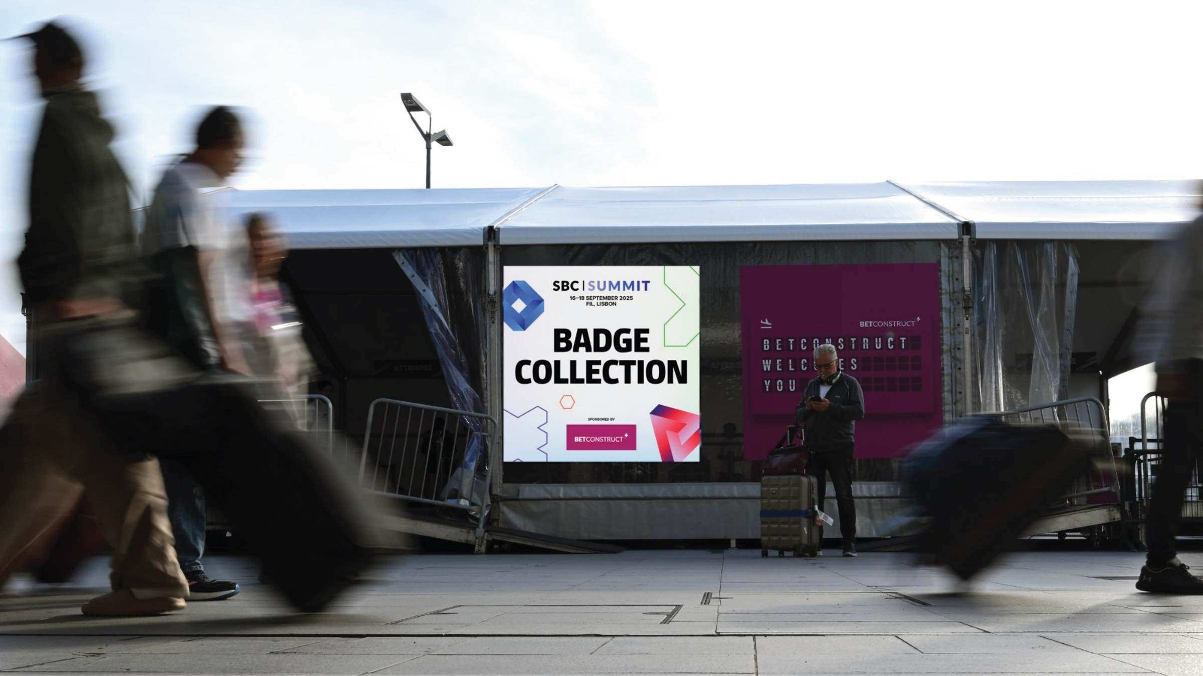 Badge collection signage at the venue entrance, with delegates walking past