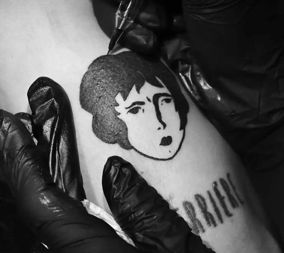 A gloved hand tattooing the Benzorella face onto skin