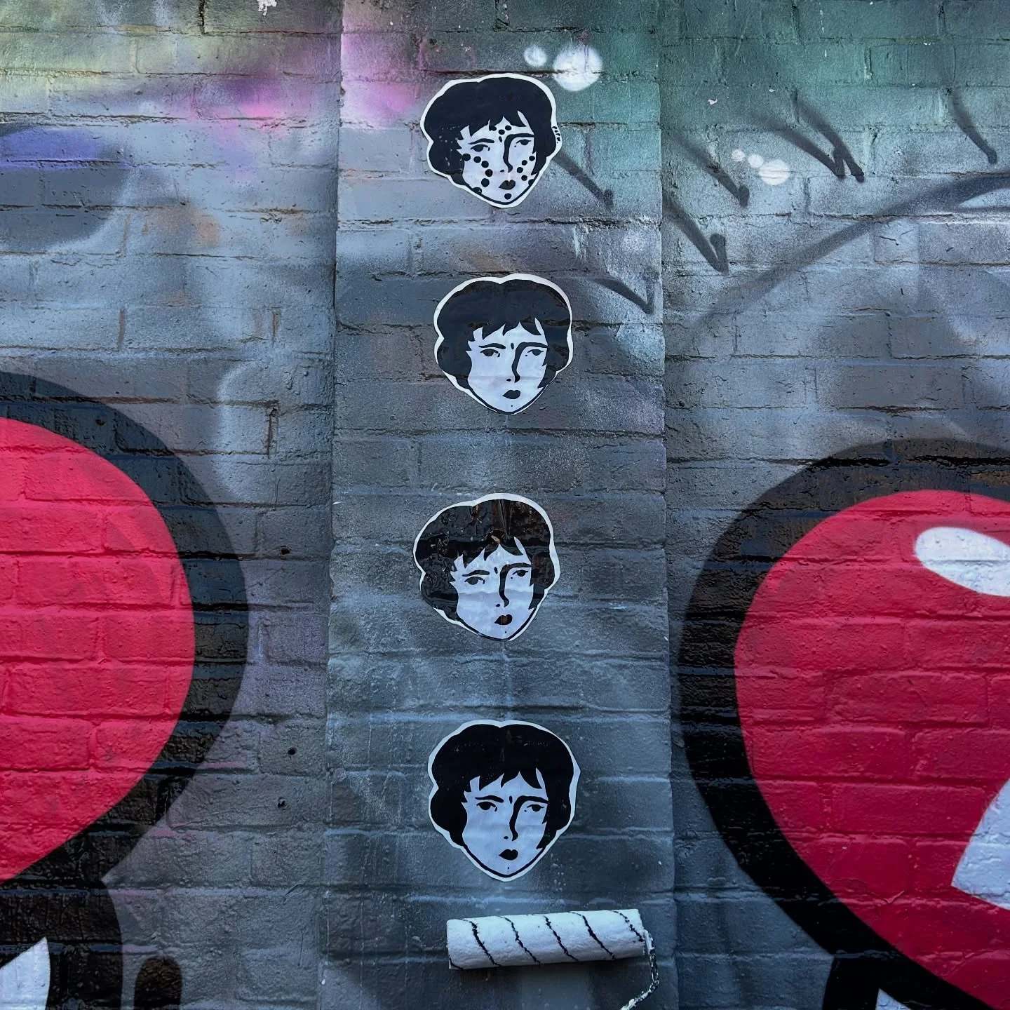 Four Benzorella faces pasted in a vertical row on a grey graffiti wall