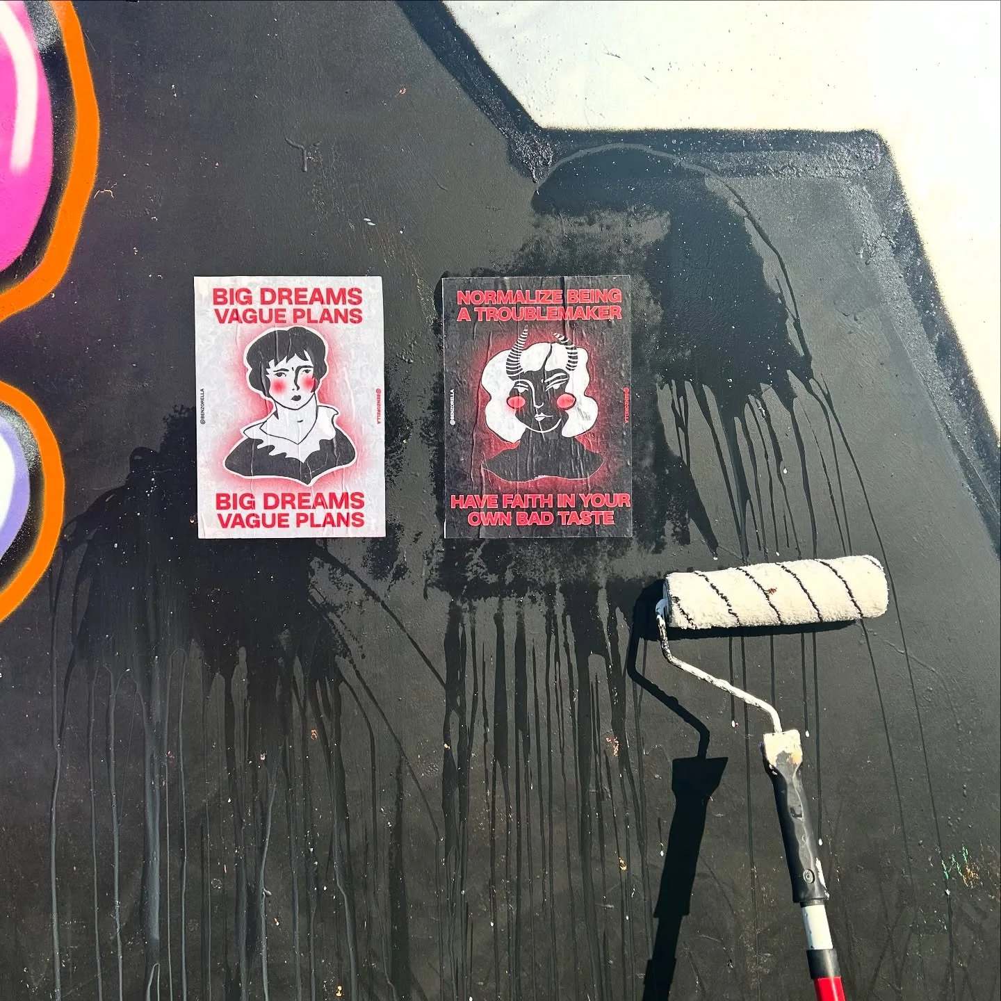 Two black posters of the Benzorella face with the line Big dreams vague plans, next to a paste roller