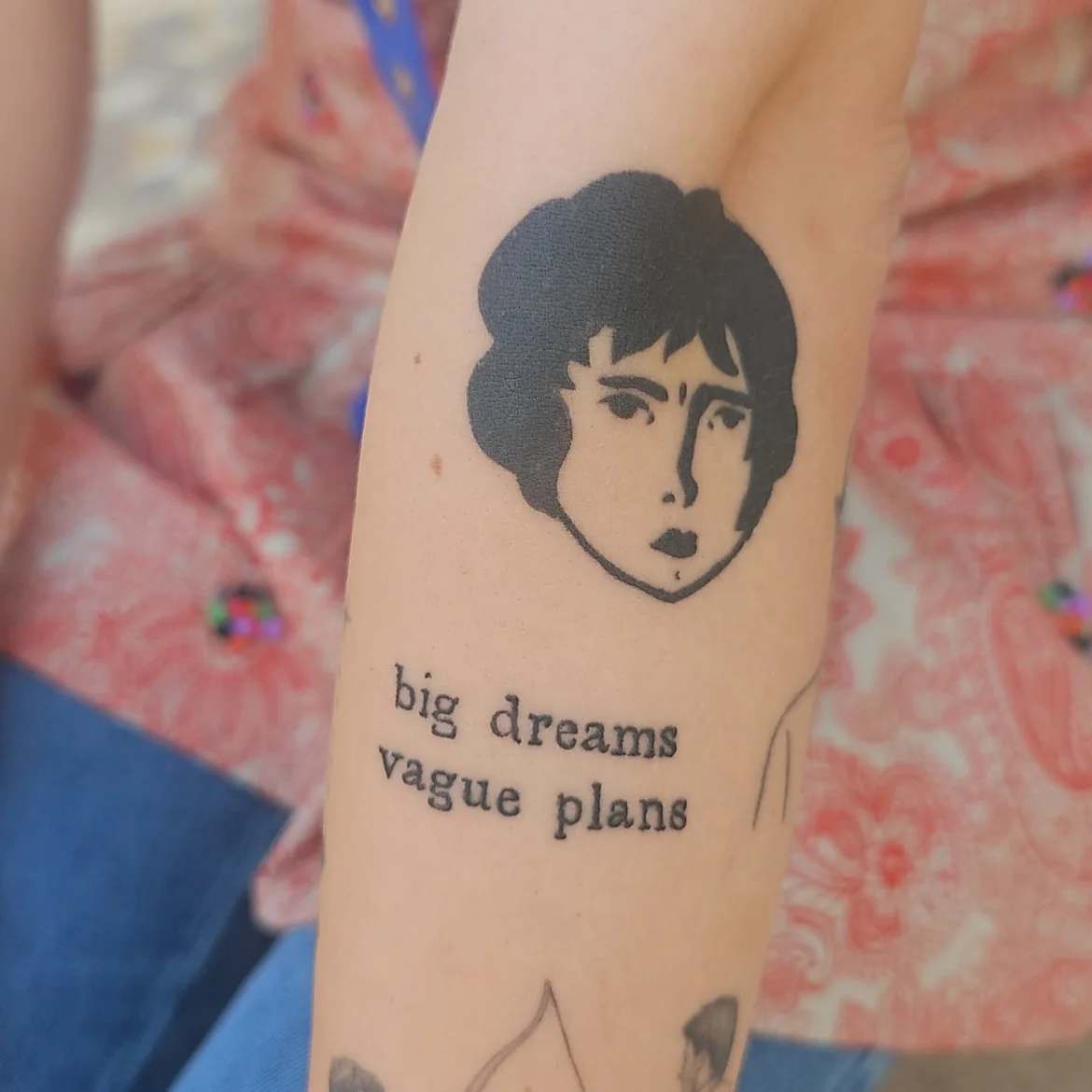 A tattoo of the Benzorella face with the text big dreams vague plans underneath