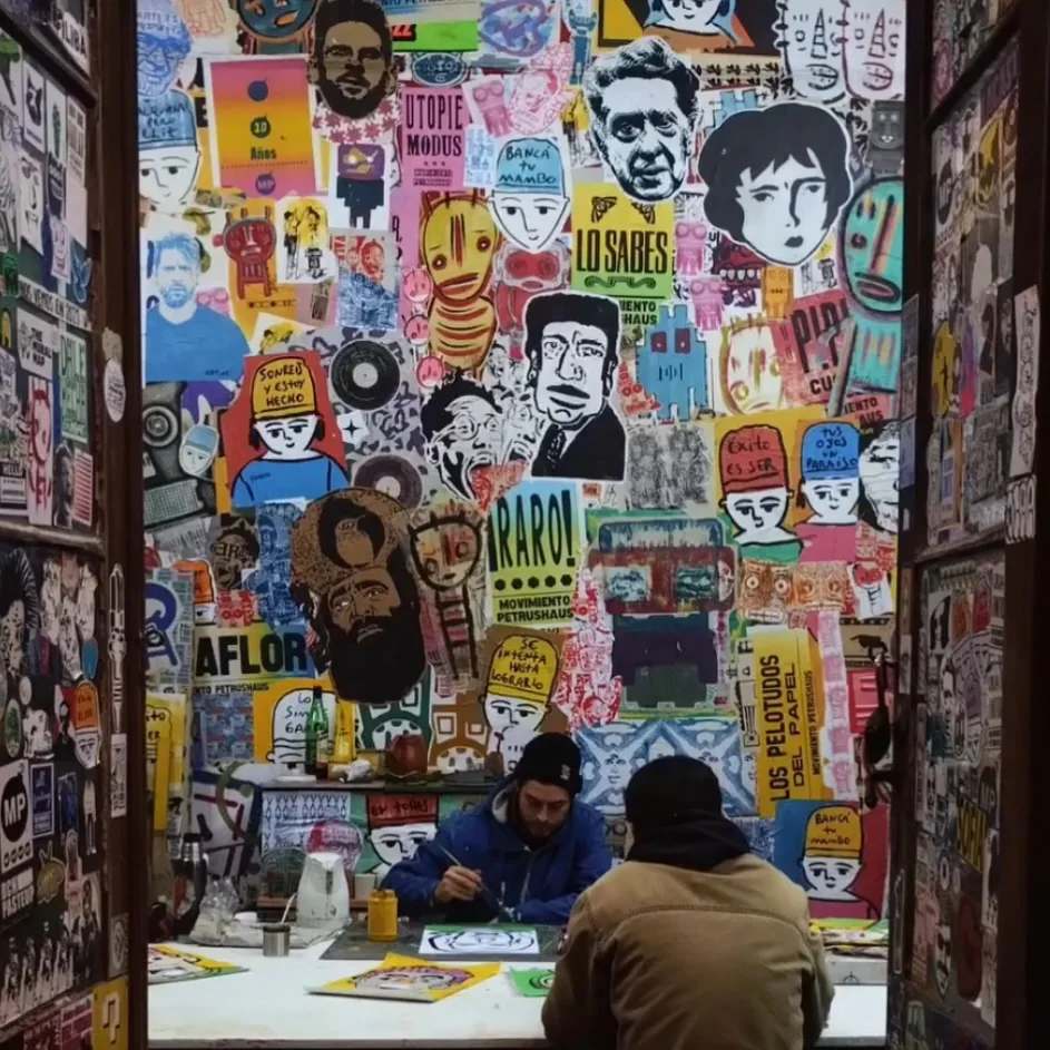 A dense sticker wall with several Benzorella faces mixed into street art