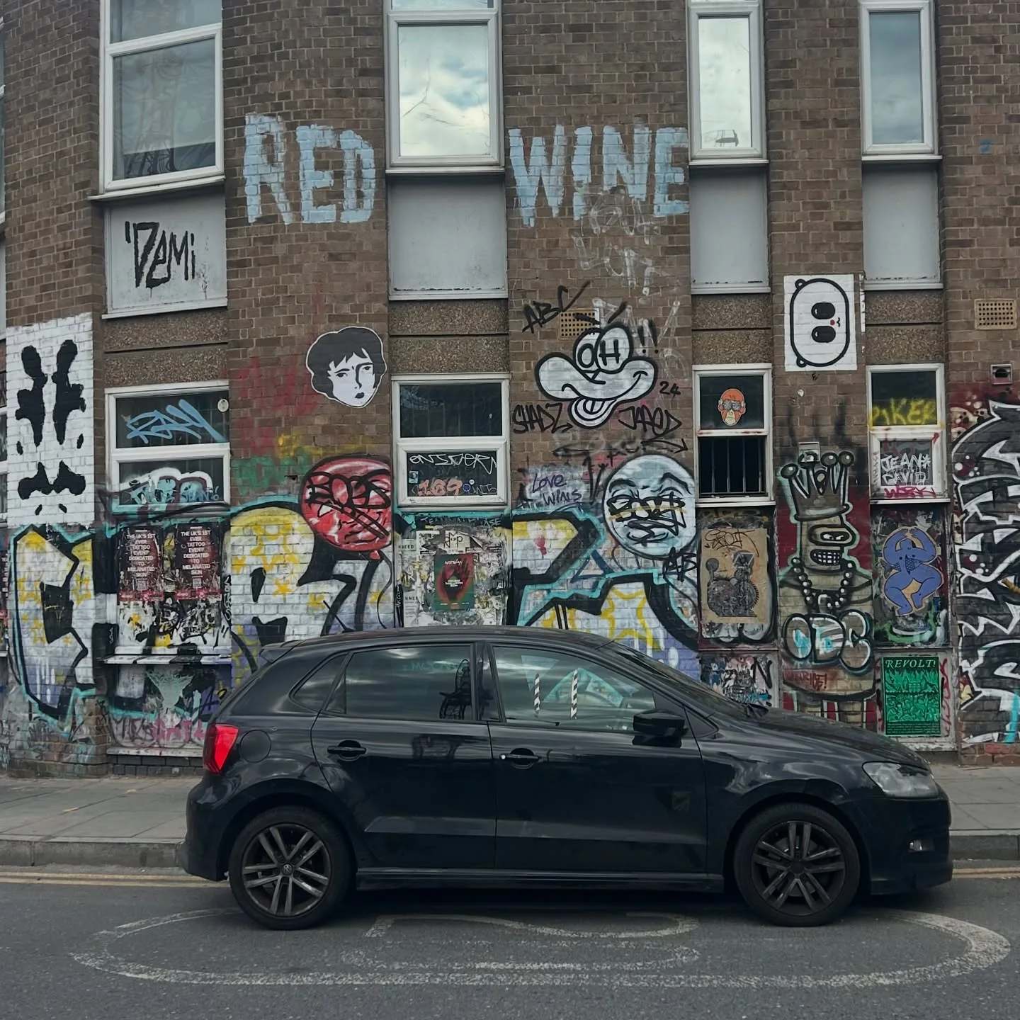 Large Benzorella wheatpastes on a brick building beside a parked car
