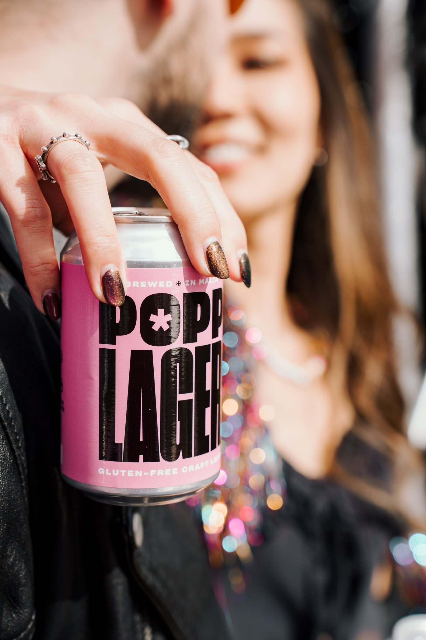 A woman holding a POPP Lager can close to the camera, softly out of focus behind it